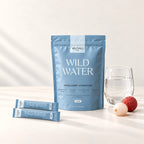 WILD WATER™ still life with pouch, two sachets, a glass of water and lychees.