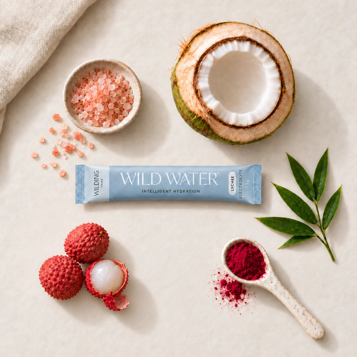 A WILD WATER™ sachet surrounded by pink salt, coconut, lychees, beetroot powder and bamboo leaves.
