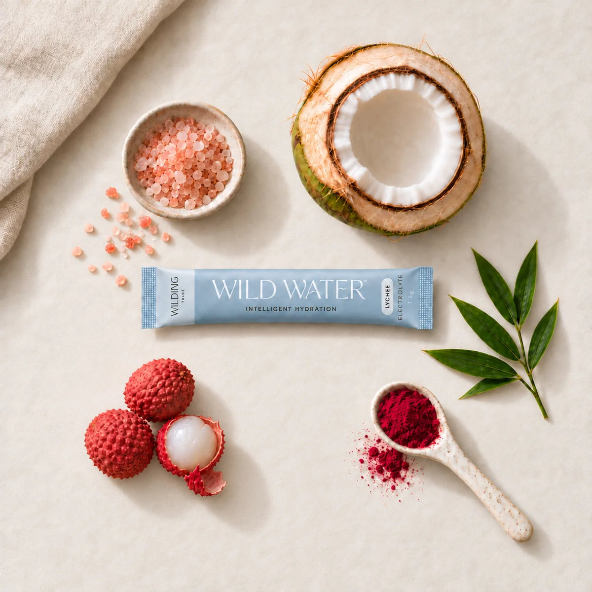 A WILD WATER™ sachet surrounded by pink salt, coconut, lychees, beetroot powder and bamboo leaves.